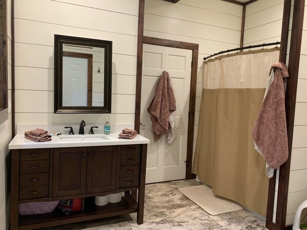 Une salle de bain avec un lavabo blanc, un meuble-lavabo en bois foncé, un miroir, un porte-serviettes, un rideau de douche et un sol en marbre.