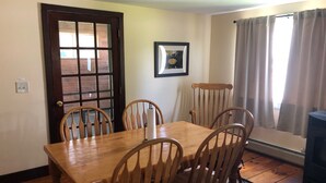 Un comedor con mesa y sillas de madera, un cuadro en la pared y una ventana con cortinas.