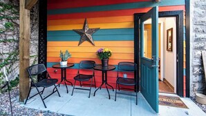 Un mur extérieur aux couleurs vives, orné d’une étoile décorative, une pergola en bois et un petit espace de détente extérieur avec des chaises et une table.