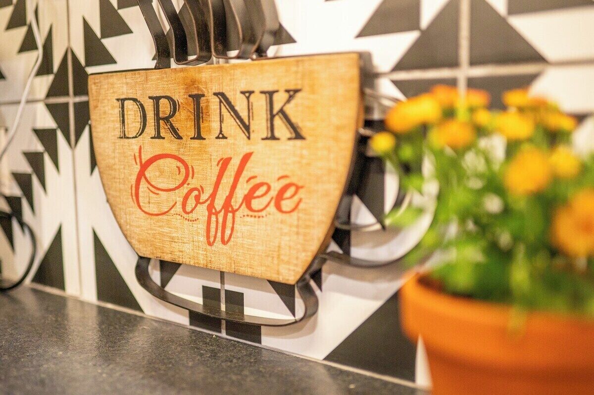Une enseigne en bois portant l’inscription « BUVEZ du café » est fixée à un mur.