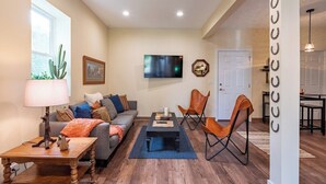 Un salon comprenant un canapé, une table basse et des fauteuils, un téléviseur à écran plat et un cactus.