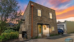A small stone building with a green door and a garage door, surrounded by greenery and a parked car. - Downtown Lake Geneva Hideaway Balcony Walk to Beach Live Music Sleeps 8 (Lake Geneva)