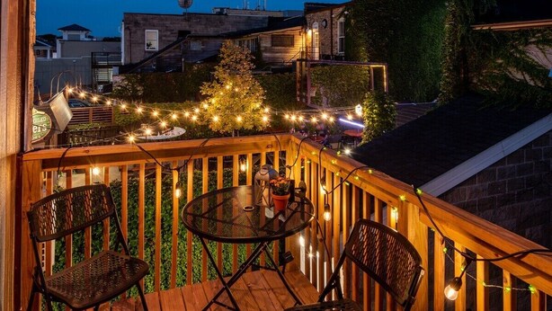 A wooden deck with a round table and two chairs, surrounded by string lights. - Downtown Lake Geneva Hideaway Balcony Walk to Beach Live Music Sleeps 8 (Lake Geneva)
