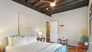 A bedroom with a bed, a hanging macrame wall hanging, a lamp, a small table, and a potted plant. - Downtown Lake Geneva Hideaway Balcony Walk to Beach Live Music Sleeps 8 (Lake Geneva)