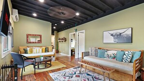 A cozy living room with a sofa, a coffee table, and a dining table. There is a TV mounted on the wall and a framed picture above the sofa. - Downtown Lake Geneva Hideaway Balcony Walk to Beach Live Music Sleeps 8 (Lake Geneva)