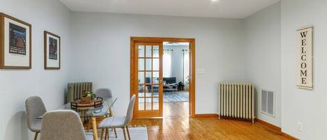 Una sala de estar moderna con una mesa de comedor de vidrio, sillas tapizadas en gris, piso de madera, un radiador y un letrero en la pared que dice 'WELCOME'.
