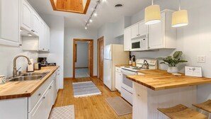 Una cucina moderna con mobili bianchi, piani di lavoro in legno, piano cottura integrato e lampade a sospensione.