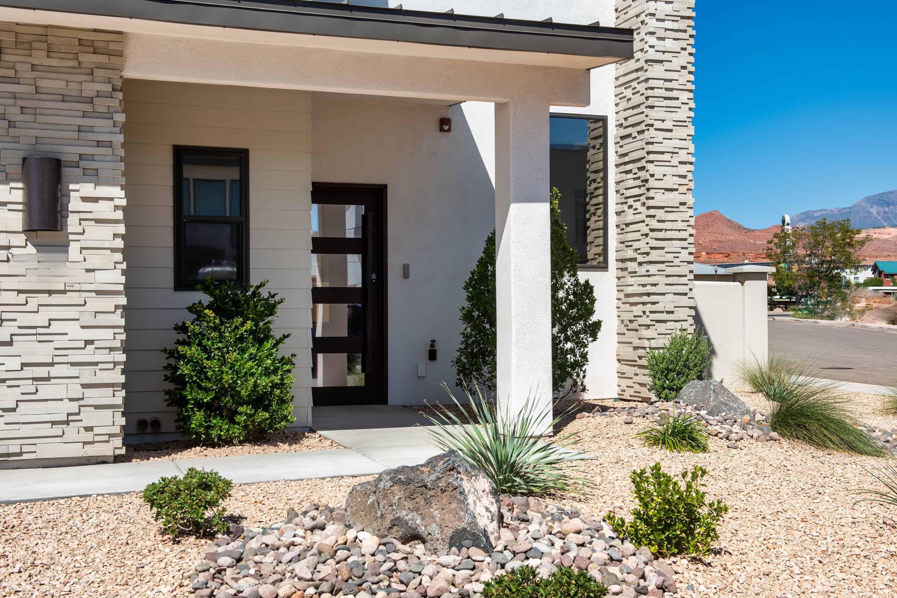 A modern house with a stone facade, a black door, and a landscaped front yard with rocks and small plants.