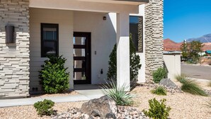 A modern house with a stone facade, a black door, and a landscaped front yard with rocks and small plants.
