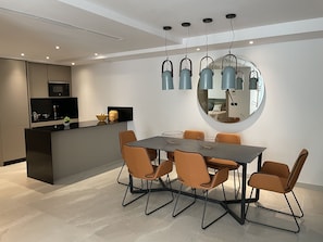 Une cuisine moderne équipée d’un four à micro-ondes encastré, un coin repas avec une table ronde et des chaises orange, et un grand miroir au mur.