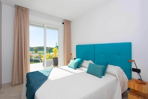 Relax in a spacious room with a large bed and sliding glass door leading to an outdoor area with lush greenery.