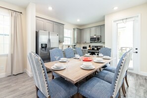 Une cuisine moderne avec des meubles gris, un réfrigérateur en acier inoxydable et un coin repas avec une table en bois, mise pour six personnes.