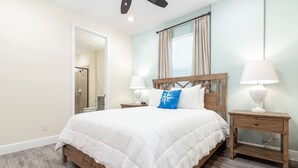A bedroom with a large bed, two bedside tables with lamps, a wooden headboard, and a window with curtains.