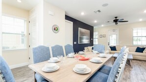 A dining area with a long wooden table set for a meal, blue upholstered chairs, and a ceiling fan.