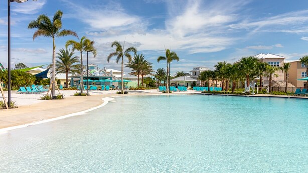 A resort pool with clear blue water, surrounded by palm trees and beach chairs.