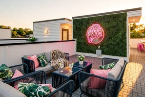A rooftop patio with outdoor seating, a neon sign, and a green wall.