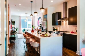 A modern kitchen with a central island, pendant lighting, and a view into the dining area. - Dolly-themed house with rooftop deck, sleeps 12, near Broadway (Nashville)