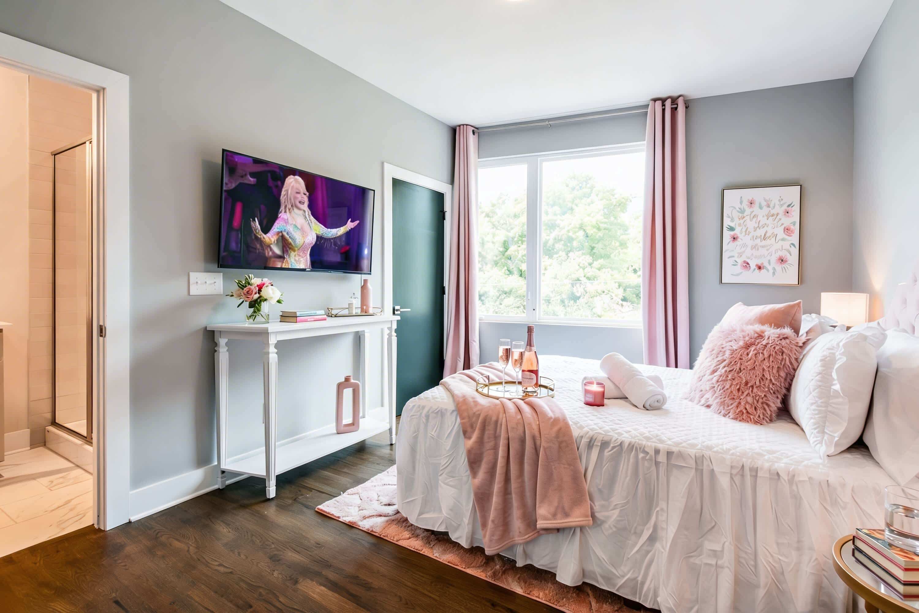 A bedroom with a bed, a TV, a desk, and a window.