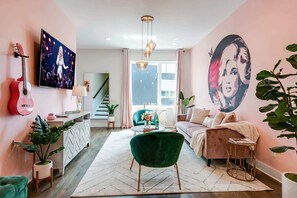 A modern living room with a pink wall, a large TV, a green chair, a sofa, and a plant. - Grand Ole Opry-themed rooftop house | sleeps 16 near Centennial Park (Nashville)