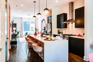 Une cuisine moderne dotée d’un îlot central, de tabourets de bar, de luminaires suspendus et donnant sur la salle à manger.