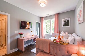 A modern bedroom with a large window, a TV, a bedside table with a bottle and glasses, and a cozy bed with pillows. - Grand Ole Opry-themed rooftop house | sleeps 16 near Centennial Park (Nashville)