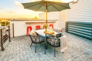 Una terraza en la azotea con una mesa, sillas, una sombrilla grande y vistas a la ciudad.