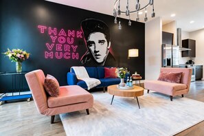 A modern living room with a neon sign, sofas, a coffee table, and a kitchen in the background. - Elvis-themed Nashville home with karaoke stage, game room & 4 bedrooms (Nashville)