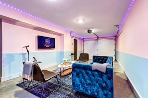 A room with a karaoke setup, a projector, a blue sofa, and a small table with drinks.