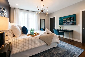 Una habitación de hotel moderna con cama, escritorio, televisor y un ventanal con cortinas.