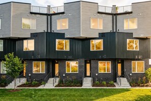 A modern multi-story residential building with a symmetrical facade, large windows, and a well-maintained lawn.
