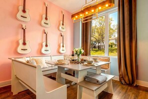 A dining area with a white table and benches, a wall with six guitars, and a window with curtains.
