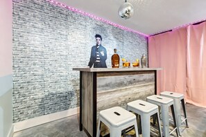 A bar area with a brick wall, a wooden bar counter, and three white stools.