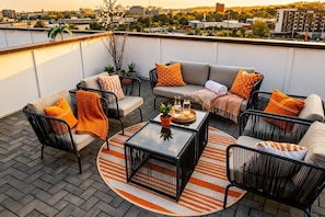 A rooftop terrace with a sofa set, chairs, a coffee table, and potted plants.