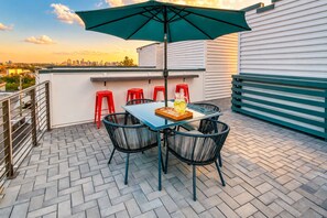 A rooftop terrace with a table, chairs, and a green umbrella.