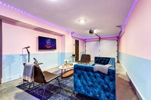 A room with a karaoke setup, a projector, a blue sofa, and a small table with drinks. - Elvis-themed Nashville home with karaoke stage, game room & 4 bedrooms (Nashville)