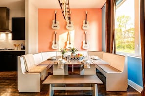 A modern dining area with a built-in bench seating, a central table, and guitars mounted on the wall.