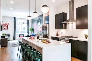 Une cuisine moderne dotée d’un îlot central, d’appareils électroménagers en acier inoxydable et de luminaires suspendus.
