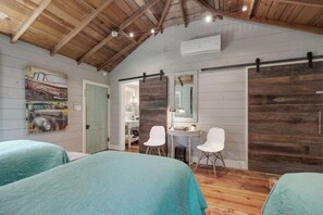 Ein Schlafzimmer mit zwei Betten, Holzboden, einem Spiegel und einem kleinen Schreibtisch mit Stühlen.