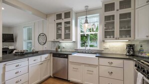 Uma cozinha moderna com armários brancos, lava-louças, pia e janela com vista para o verde.