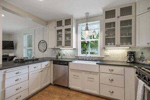 Een moderne keuken met witte kasten, een vaatwasser, een spoelbak en een raam met uitzicht op groen.