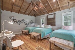 A cozy room with wooden floors, two beds with teal bedding, a desk with a lamp, and a wall decorated with metal plates.