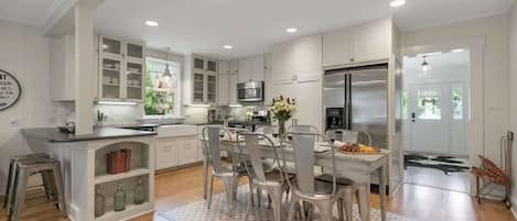 A modern kitchen with white cabinetry, a central island, and a dining area with metal chairs.
