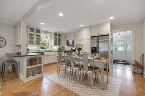 A modern kitchen with white cabinetry, a central island, and a dining area with metal chairs.