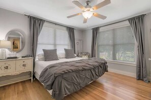 A bedroom with a bed, a dresser, a ceiling fan, and large windows with blinds. - Clover Haus 2 Blks to Main/Pool & Hot-Tub! (Fredericksburg)