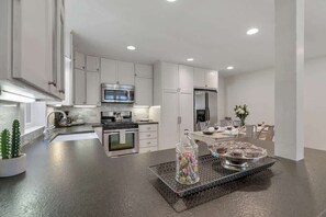 Una cocina moderna con gabinetes blancos, electrodomésticos de acero inoxidable y una isla central con un frasco de vidrio lleno de caramelos.