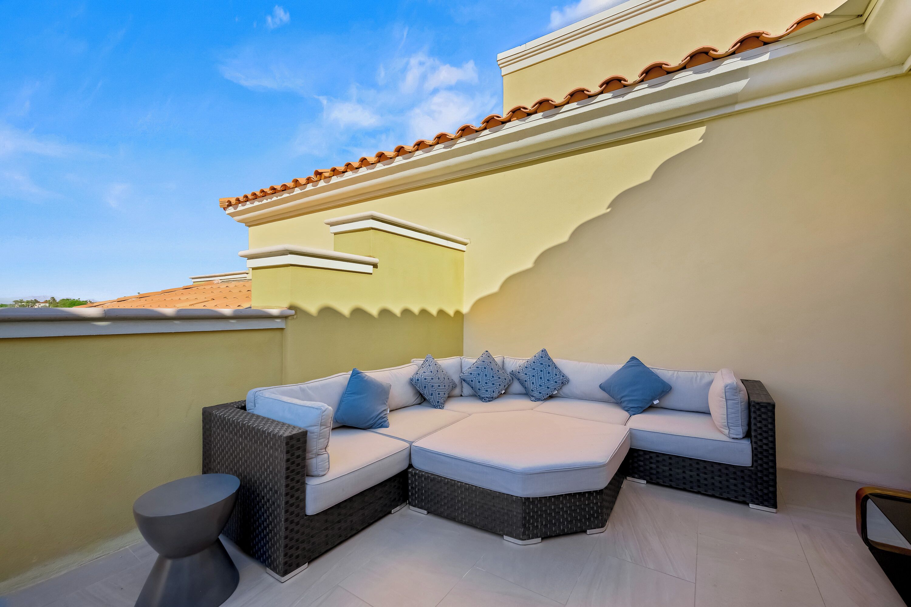A corner seating area with a white sofa and wicker chairs, a small round table, and a tiled roof.