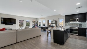 A modern kitchen with a central island, a dining area with a large table, and a living room with a sofa and TV.