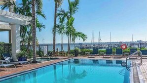 Una piscina con sillas de descanso, palmeras y vistas al puerto deportivo.