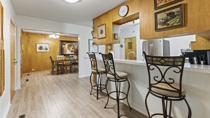 Une cuisine avec des meubles de rangement en bois, un réfrigérateur et un coin repas comprenant des chaises et une table.