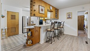 Une cuisine de taille réduite dotée d’un îlot central, d’appareils électroménagers en acier inoxydable et de meubles de rangement en bois.